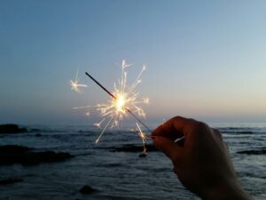 hand holding sparkler with ocean in the background