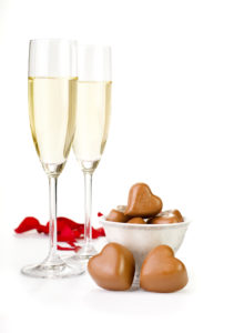 Romantic table decoration with rose petals, champagne and chocolates on a white background